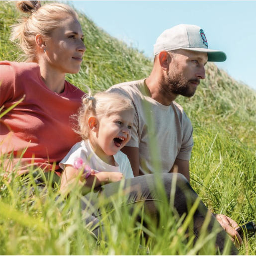 A man, woman, and child sitting on a grassy hillside, enjoying a peaceful moment outdoors, reflecting the comfort and natural lifestyle behind By Zoe’s Peruvian-made textiles.