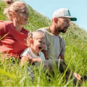 Smiling woman sitting in tall grass with her family enjoying a sunny day outdoors.