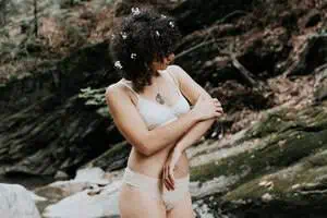 Model outdoors wearing sustainable organic cotton underwear, standing by rocks in a natural forested area.