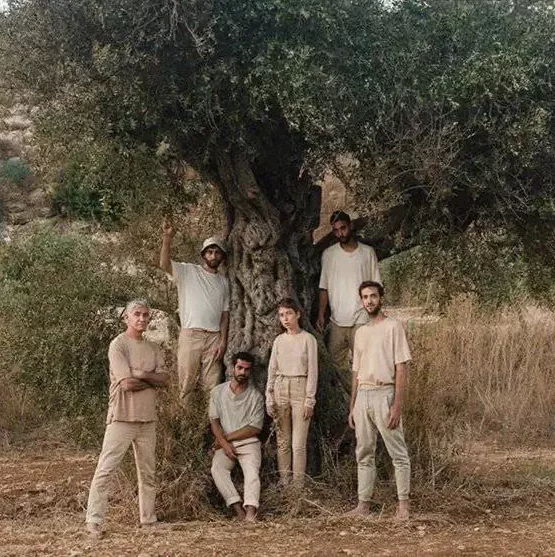 Group of people wearing earthy-toned organic cotton clothing standing under an old tree in a rural landscape.