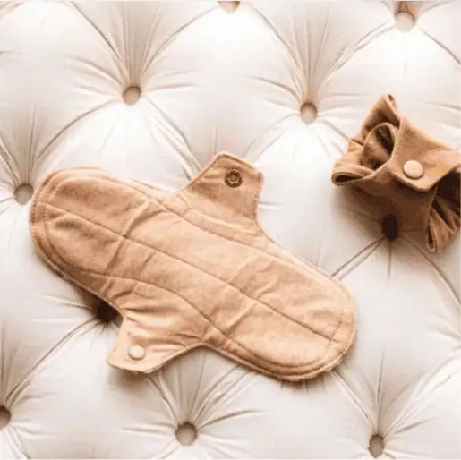 Reusable natural colored cotton pad placed on a white tufted cushion beside a rolled pad.