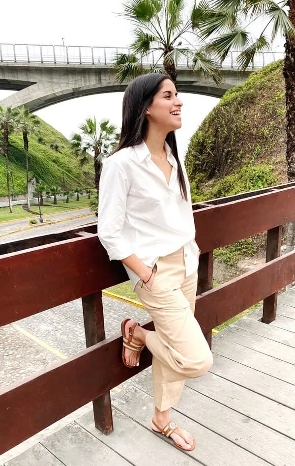 Young woman in sustainable fashion outfit leaning on a bridge in an urban green area.