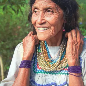 Elderly woman in traditional dress smiling and wearing beaded jewelry outdoors.