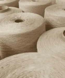 Close-up of beige-colored yarn spools made from natural fibers stacked in rows.