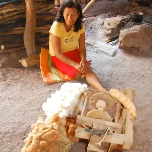 Woman in traditional dress spinning brown cotton yarn inside rustic Amazonian home.